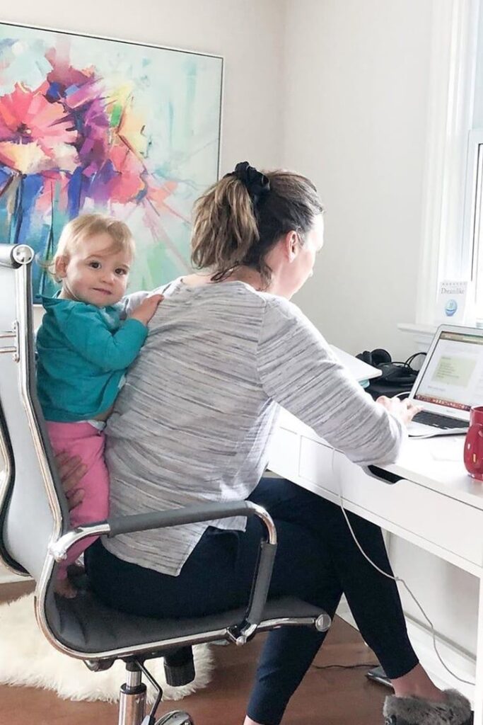 mom working on a laptop while her baby is playing at her back