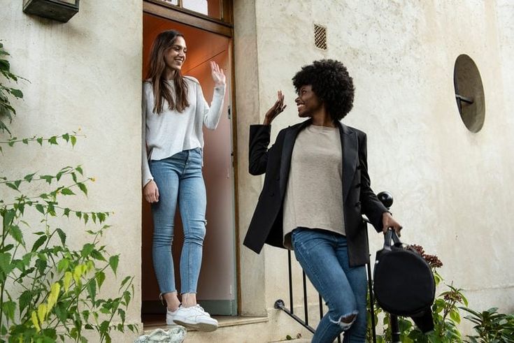 A guest waving goodbye to her friend as she leaves happily with her luggage