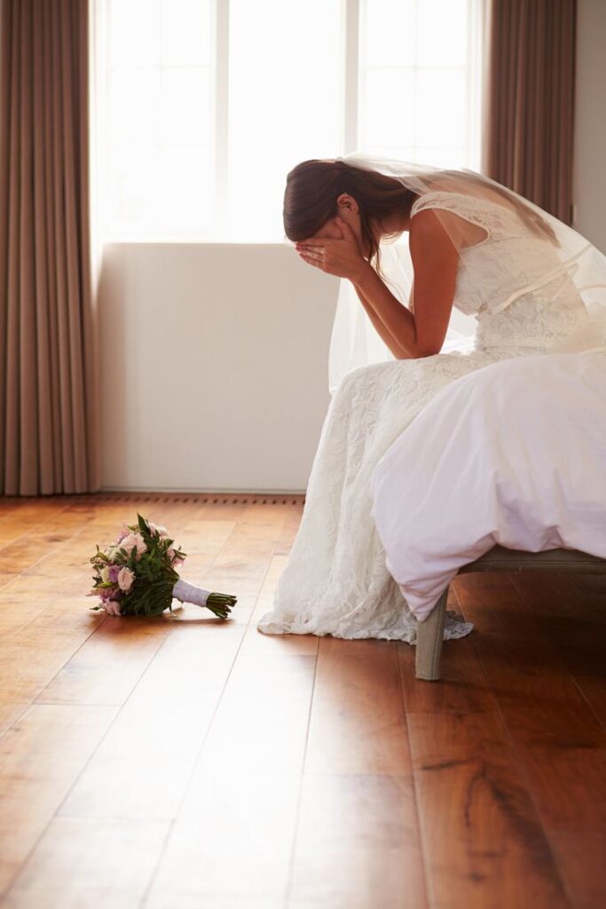 Bride sitting alone in a room with her hands on her head, appearing worried