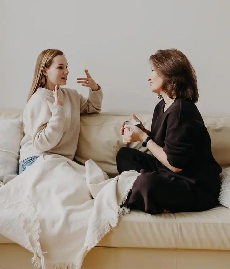 Two women sitting and chatting together, One is carrying a mug and listening while the other is speaking