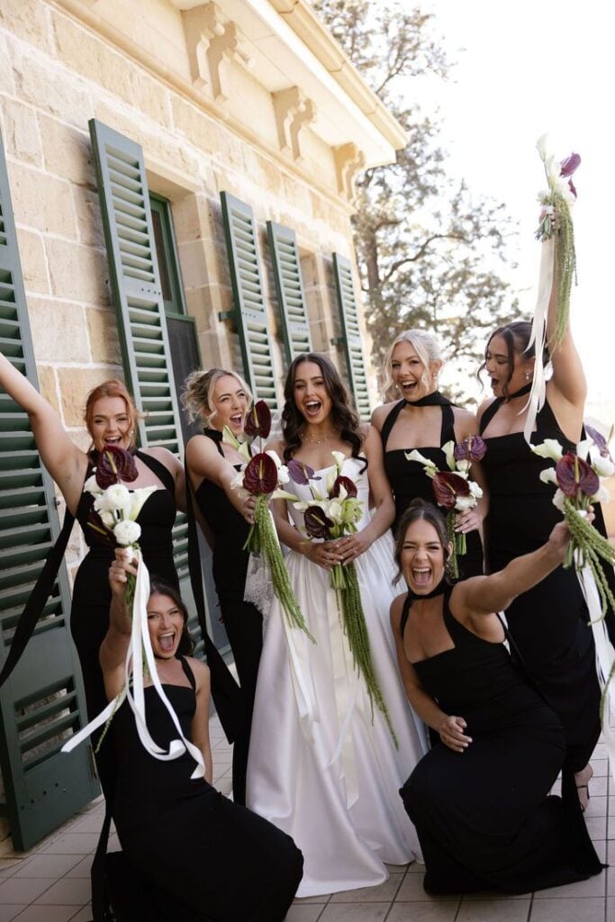 A happy bride on her white wedding dress with her bridesmaid on black dresses