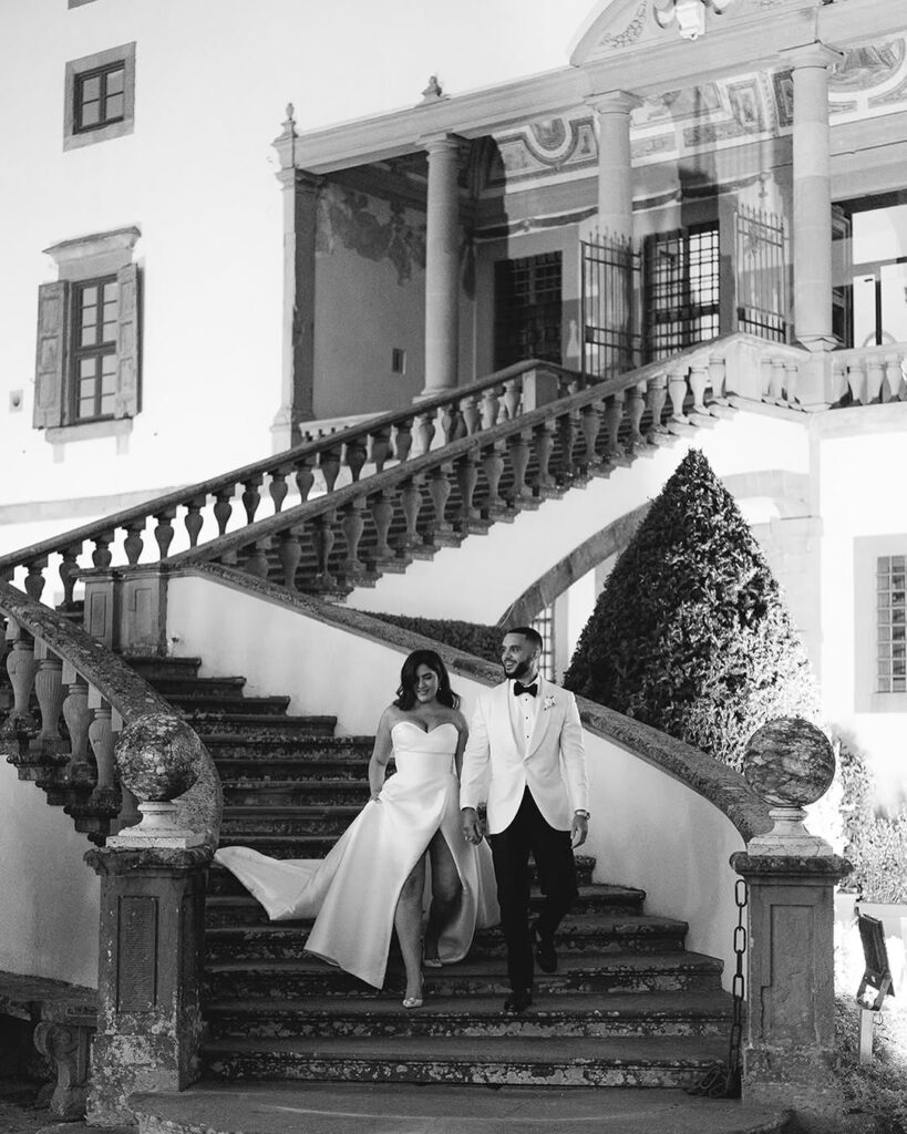 Bride and groom walking hand in hand down a grand stone staircase outside an elegant historic wedding venue.