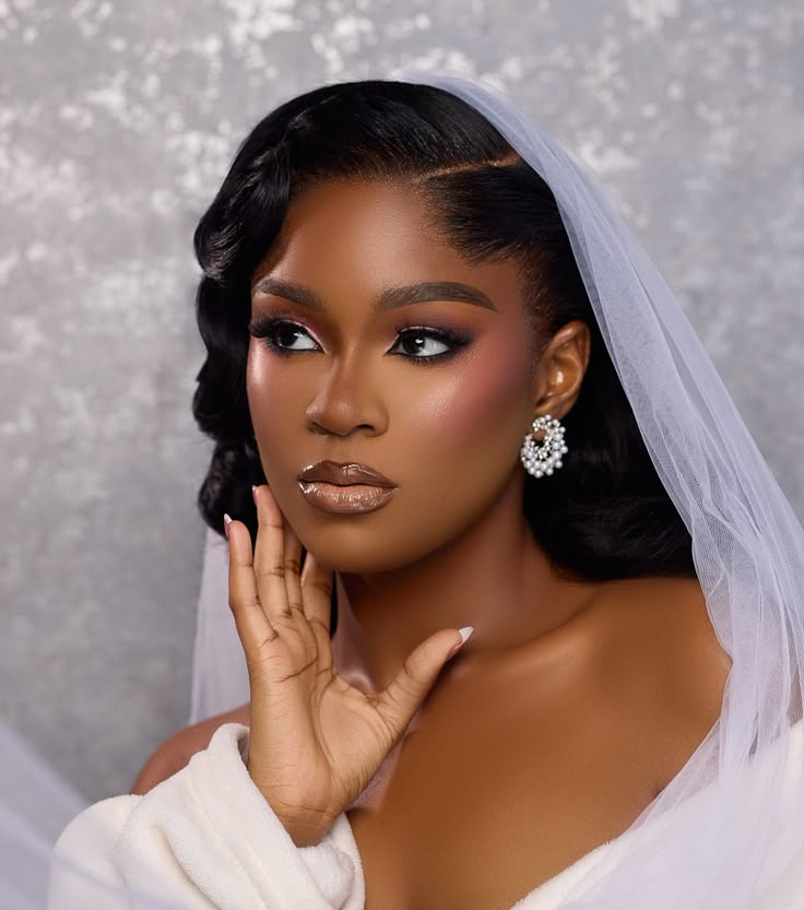 Elegant bride with radiant glam makeup featuring soft smokey eyes, glowing skin, glossy nude lips, voluminous lashes, and a classic white veil with sparkling crystal earrings.