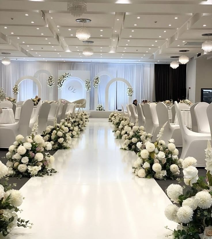 Modern contemporary chic wedding reception featuring a sleek white aisle, elegant white floral arrangements, minimalist ceremony arches, crystal chandeliers, and sophisticated all-white décor in a luxury ballroom.
