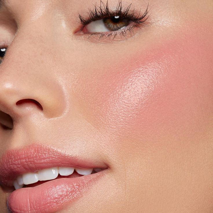 Close-up of glowing skin with soft pink cream blush, fluttery lashes, luminous highlighter, and glossy nude lips for a fresh, radiant makeup look.