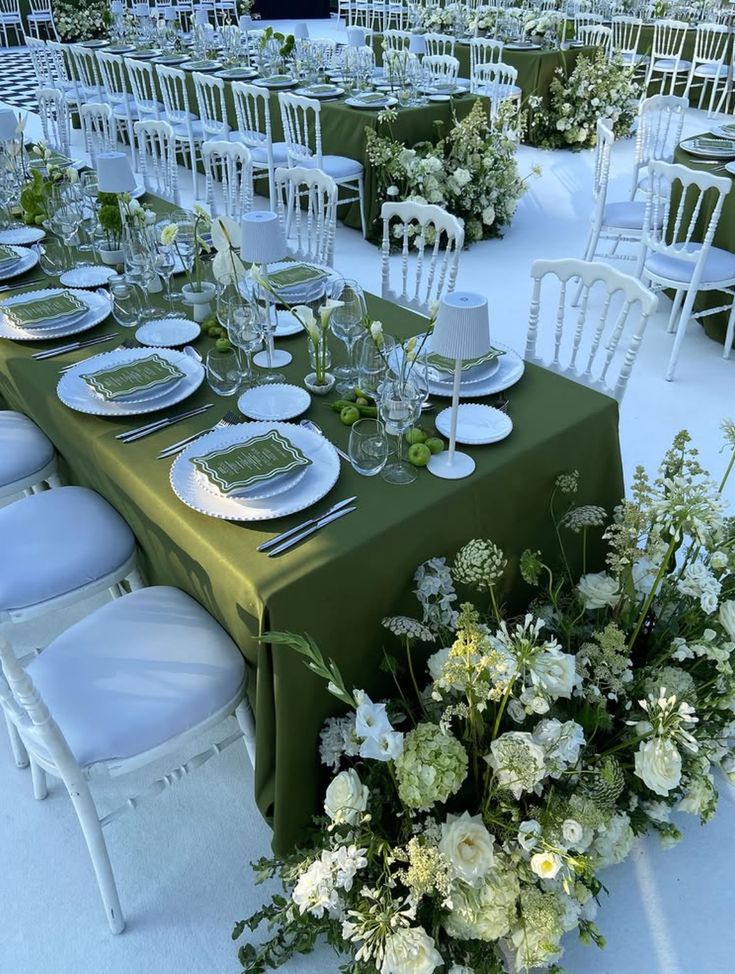 Elegant wedding reception featuring monochromatic green tablescapes with olive-green linens, white floral arrangements, layered place settings, and white chairs for a sophisticated outdoor celebration.