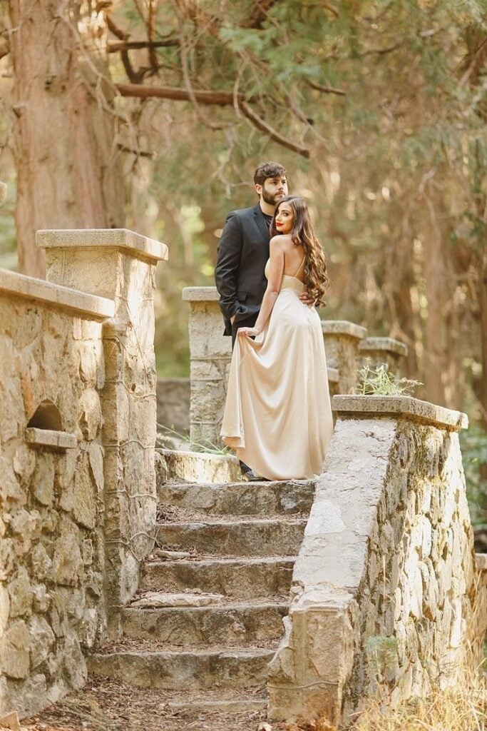 Bride and groom posing on rustic stone steps in a forest during a romantic outdoor wedding photo session.