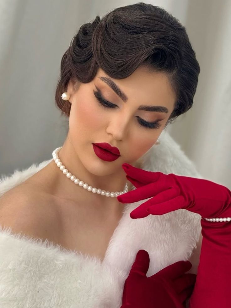 Bride with vintage-inspired glam makeup featuring bold red lipstick, dramatic winged eyeliner, soft smokey eyes, defined brows, pearl jewelry, and elegant finger waves.