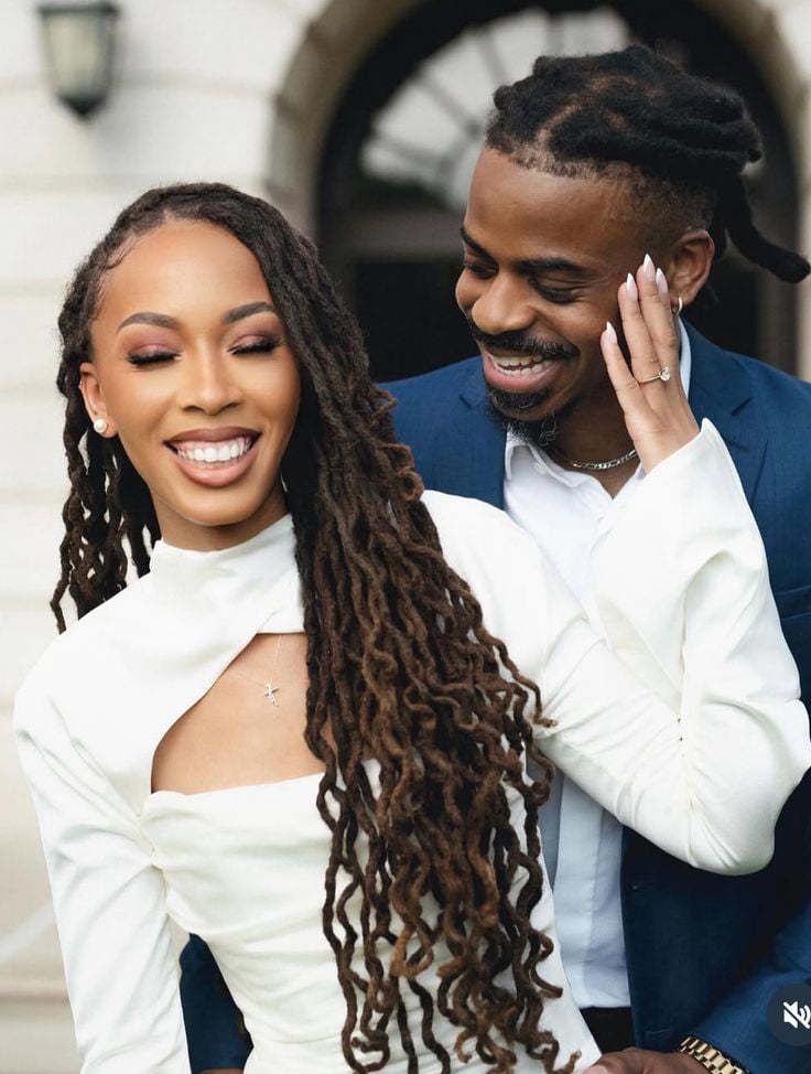A bride on long flowing locs and the groom holding her waist from behind as they smile