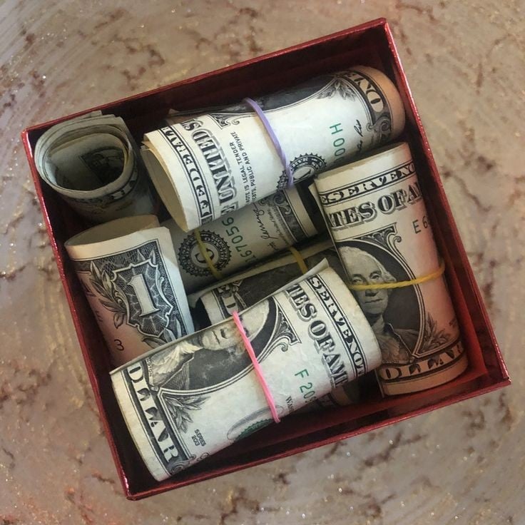 Stack of folded paper money held together with a rubber band inside a box