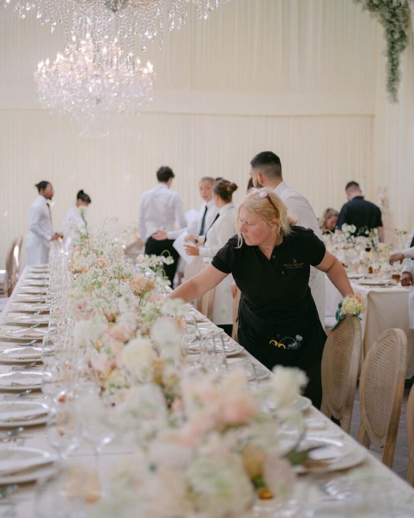 Wedding planner making final adjustments to an elegant wedding reception table with floral centerpieces and place settings.
